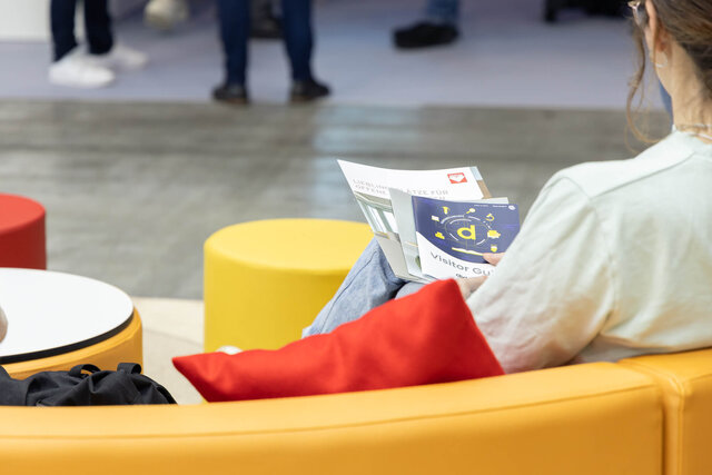 Eine Besucherin der Didacta sitzt auf einem Polstermöbel von ASS Einrichtungssysteme und hält Flyer in den Händen