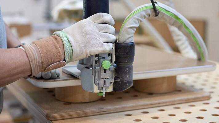 Produktionsmitarbeiterin schleift Möbel-Element aus Holz an Kantenfräsmaschine