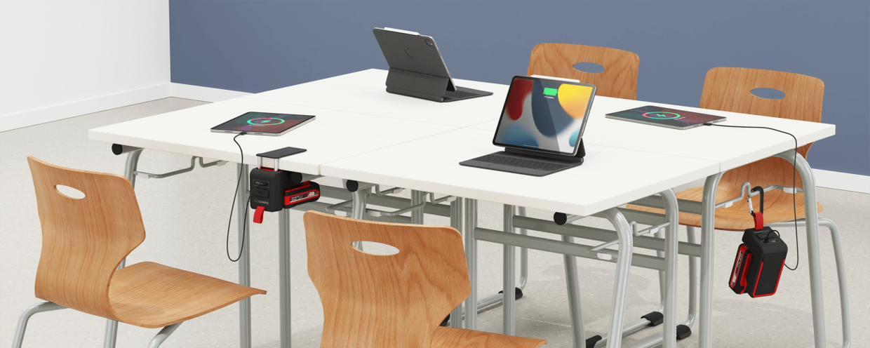 Schultisch mit einem an die Tischplatte geklemmten und einem am Mappenhaken aufgehängten FLEXCHARGE Akkuladegerät; beide laden je ein iPad auf.